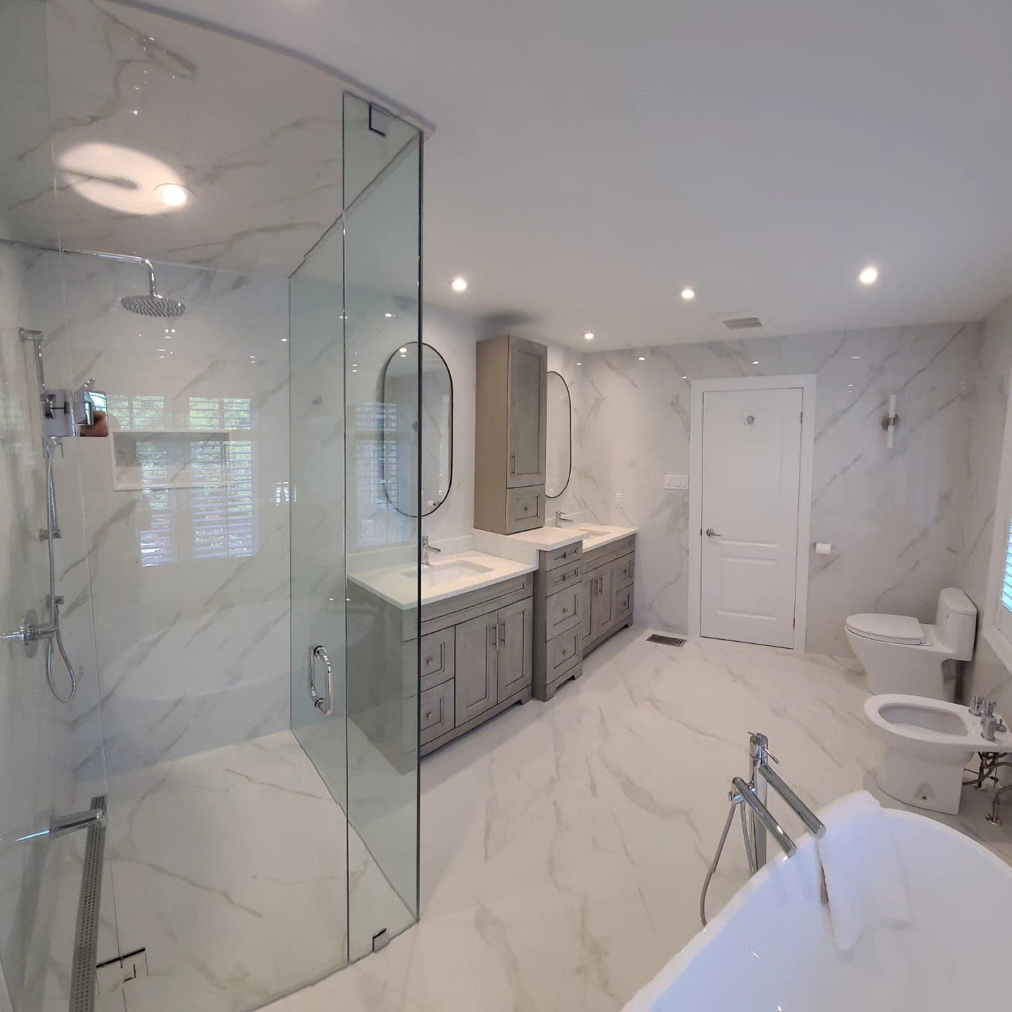 Finished master bathroom with Calacatta marble walls and floor, curved glass walk-in shower, double vanity with grey shaker cabinets, freestanding tub — by Blue Tile & Marble Toronto