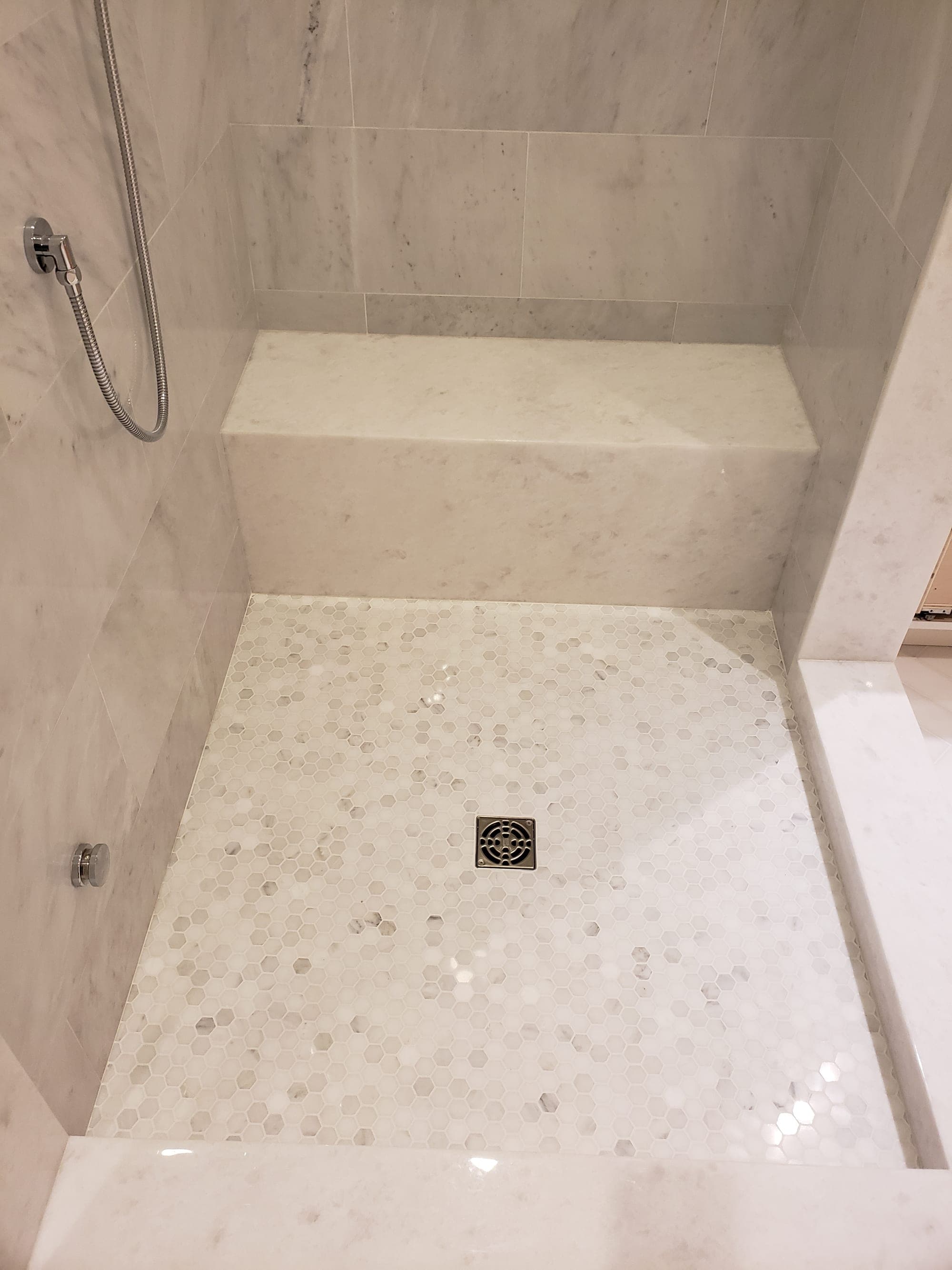 Detail of marble bench seat above hex marble mosaic shower floor with linear drain