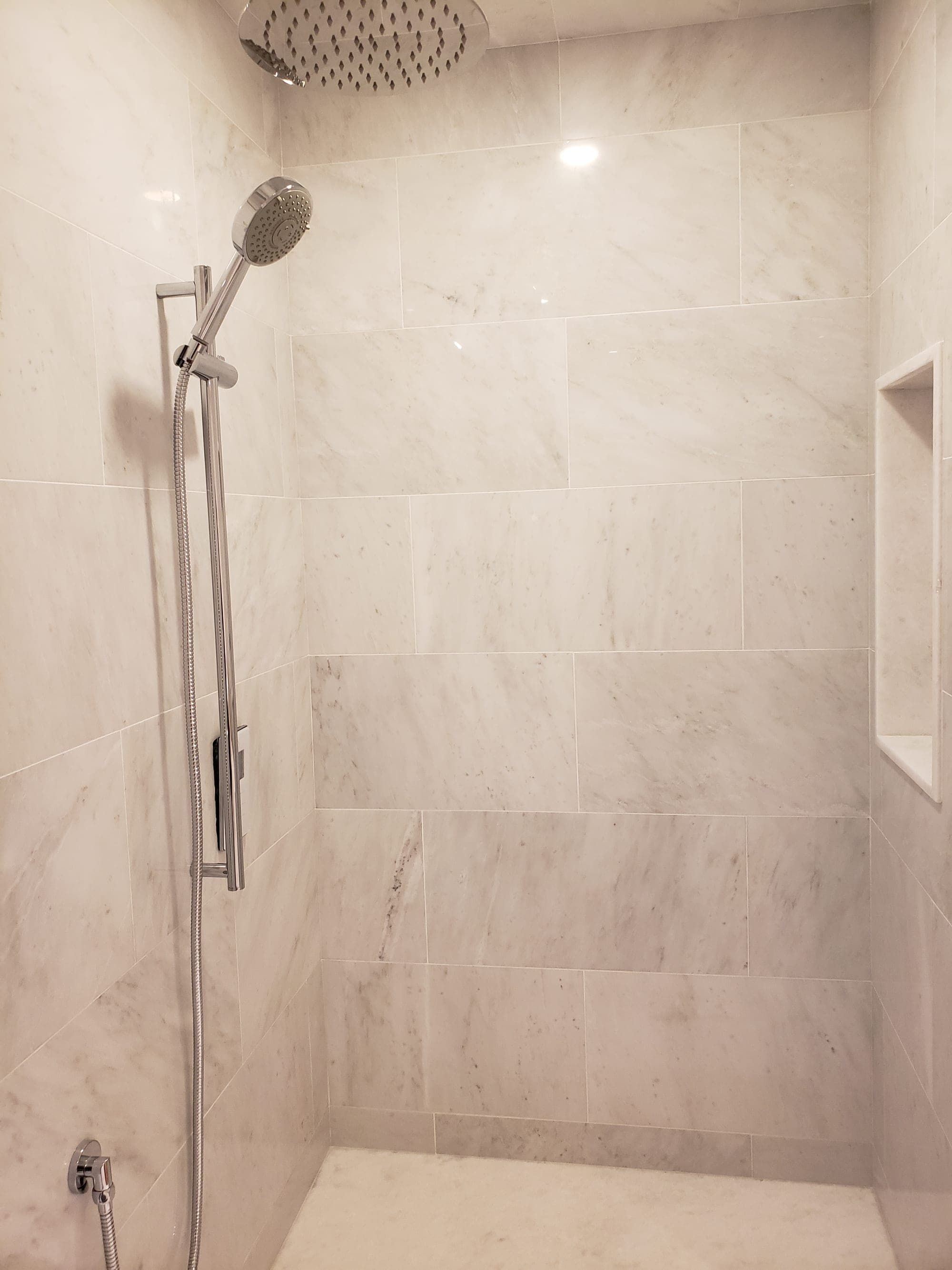 Marble shower wall with niche detail and slide-bar handheld shower