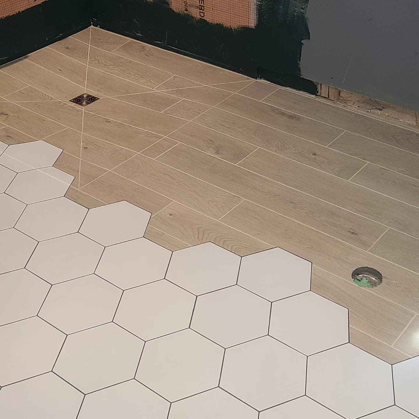 Mixed-format tile floor — large white hex tile transitioning to wood-look plank tile with brass drain — installed by Blue Tile & Marble