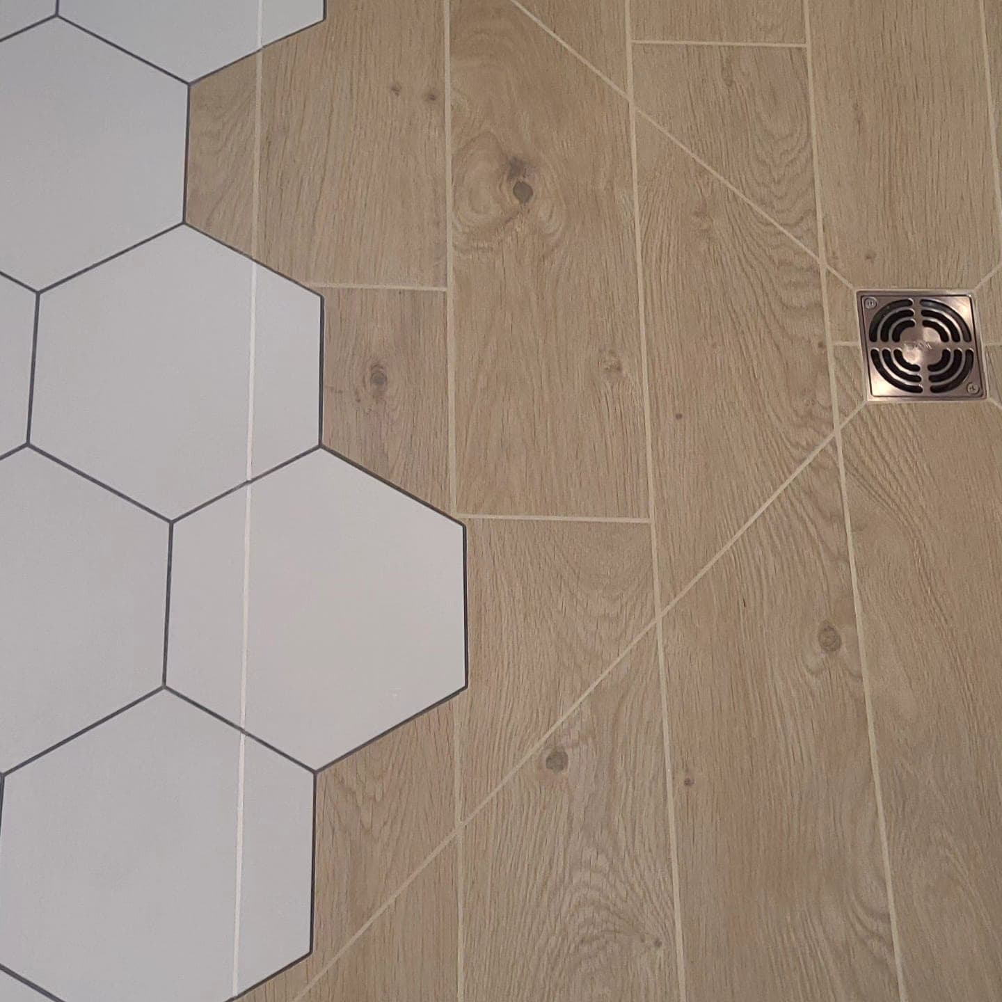 Detail view of hex tile and wood-look plank tile transition with stainless drain